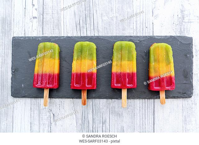 Row of four homemade fruit smoothie ice lollies on slate