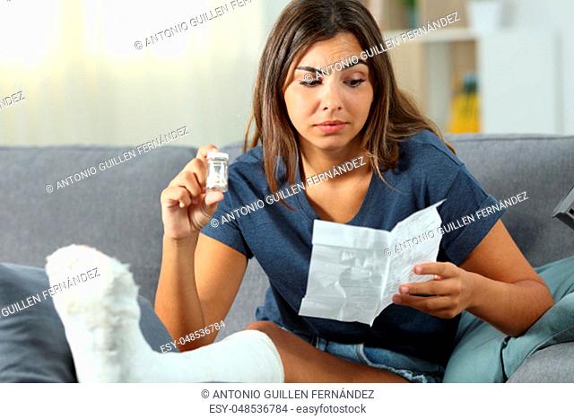 Confused disabled girl reading a leaflet of painkiller pills sitting on a couch in the living room at home