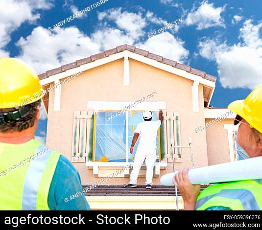 Male and Female Contractors Overlooking Painter Painting House