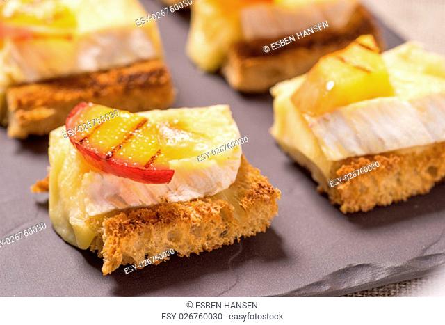 canapes, Appetizer with grilled brie and nectarine plated on a slate dish