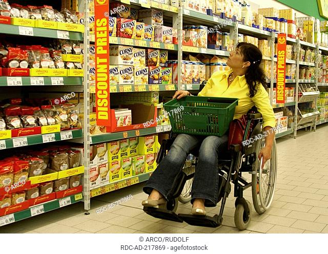 Woman in invalid chair at rack in super market, shopping basket