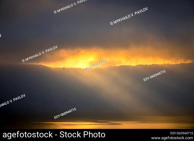 Heavy clouds over the rocky shore. Sunrays barely break through, illuminate small houses and the water surface