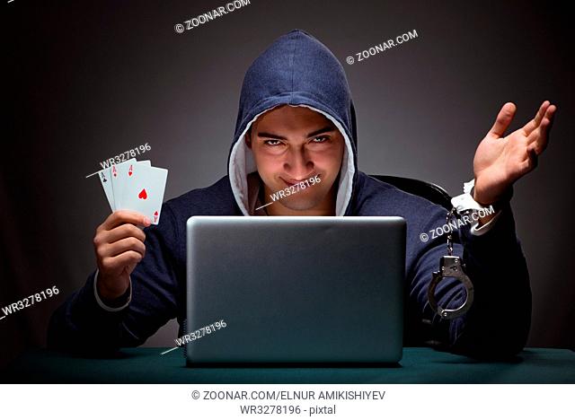 Young man in handcuffs wearing a hoodie sitting in front of a laptop computer gambling