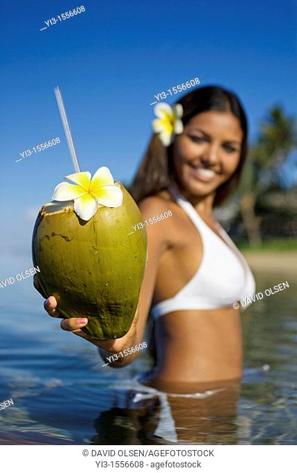 Smiling, attractive local girl holds out a coconut with straw and flower ready to drink at Lahaina, Maui, Hawaii
