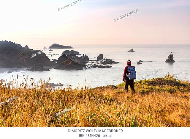 Female hiker looking out for coastal scenery with many rugged rocky islands, Whaleshead, Samuel H. Boardman State Scenic Corridor, Oregon, USA