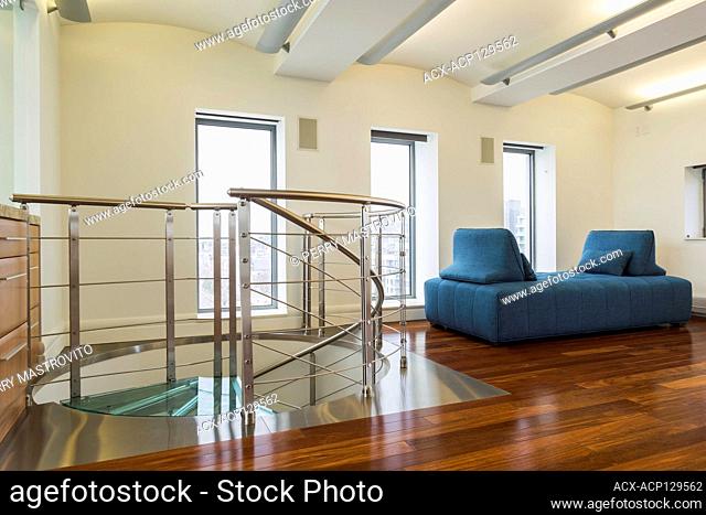 Steel and tempered glass spiraling staircase with blue cloth upholstered daybed in home office with exotic wood cabinet and floor on top floor inside a modern...