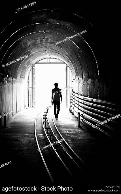 Silhouette of a young man walking out of a dark tunnel into a bright light