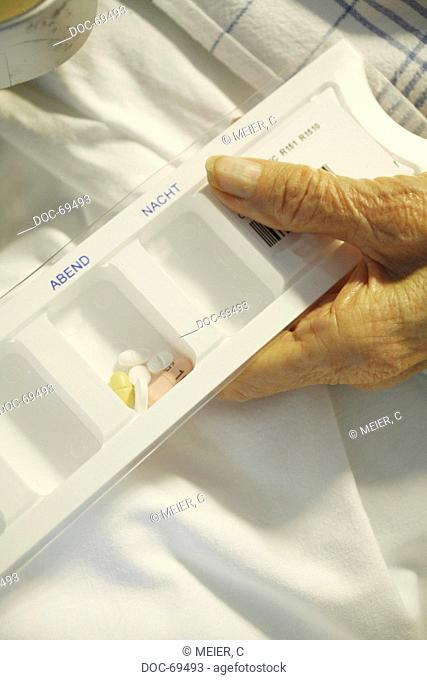 A box of tablets is lying on a bed, hold by the hand of an elderly woman