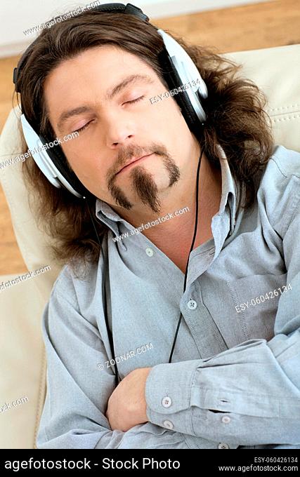 Casual man lying on couch at living room and listening music with headphones