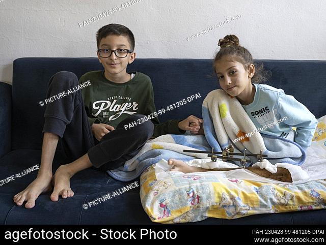 24 April 2023, Turkey, Antakya: Mehmet holds the hand of his sister Saadet while they both sit on a couch in the house of relatives