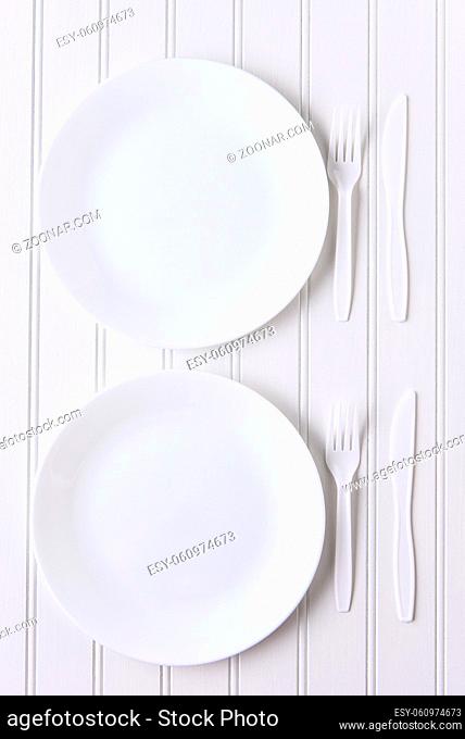 Top view of an all white place setting. White plates and plastic utensils on a white background