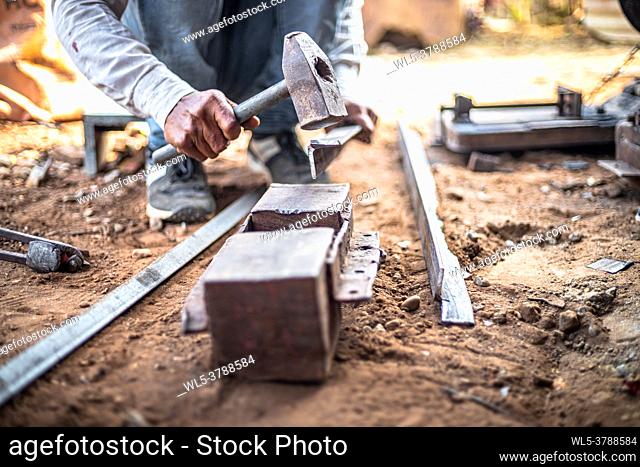 Closeup hands of a blacksmith hits iron or steel sheet with a hammer at a workshop outdoors