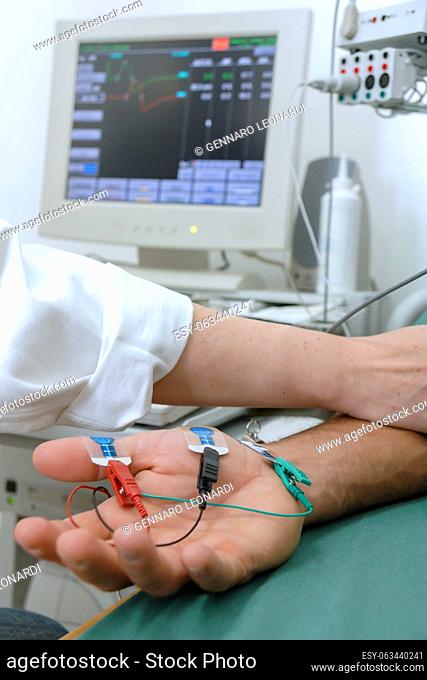 A doctor performs laboratory tests by applying electrodes to the arm of a patient lying on the table. In the background electronic equipment to monitor the test...