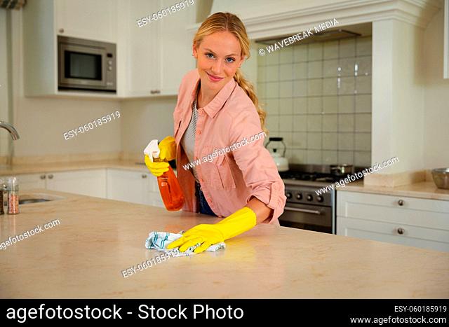 Portrait of smiling caucasian woman wearing rubber gloves cleaning kitchen worktop