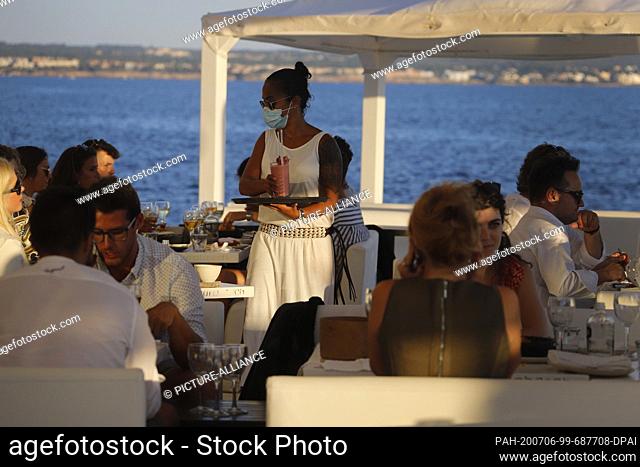 23 June 2020, Spain, Palma: A waitress with a face mask serves the customers of the Bar Purobeach in Cala Estancia on the beach Playa de Palma
