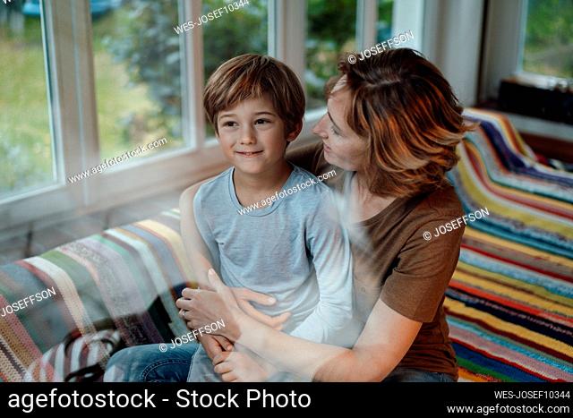 Smiling woman with son sitting on sofa at home