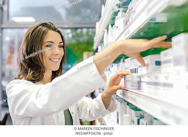 Smiling pharmacist sorting medicine at shelf in pharmacy