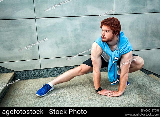 Young adult man in sportswear doing fitness exercise in the city street over gray concrete background. Outdoor sports clothing and shoes, urban style