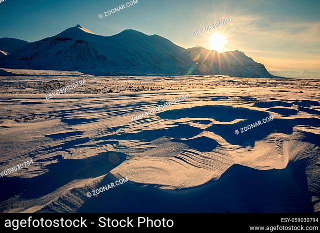 Arctic winter landscape at Kapp Ekholm, stones in the foreground, with snow covered mountains and blue sky in the background