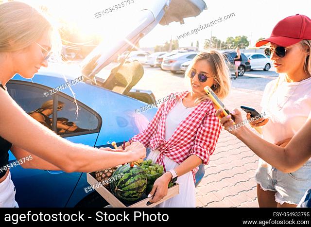 Girls hold a fruit tray and prepare a festive firework on car parking