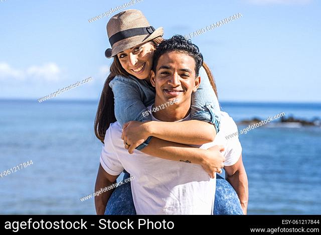 Carefree couple spending leisure time together outdoors, man giving piggyback ride to beautiful girlfriend in front of seascape during summer holiday