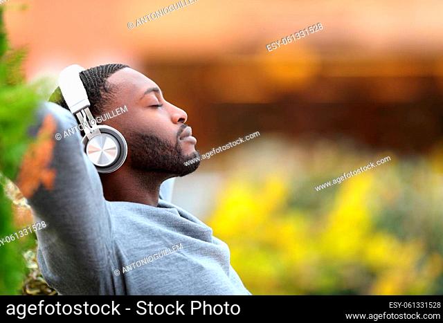 Side view portrait of a man with black skin relaxing listening to music with headphones in a park