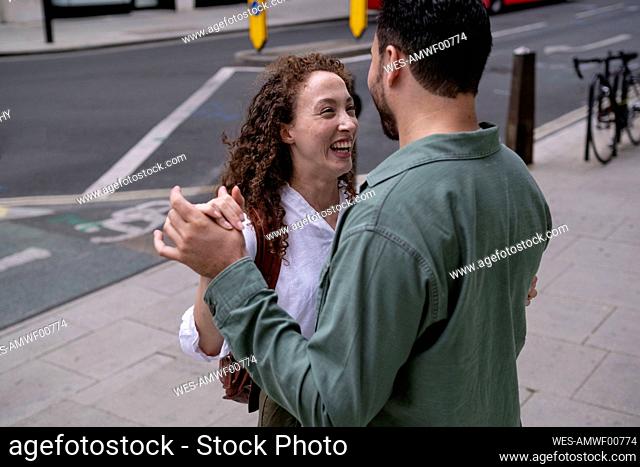 Cheerful young woman with man dancing on footpath