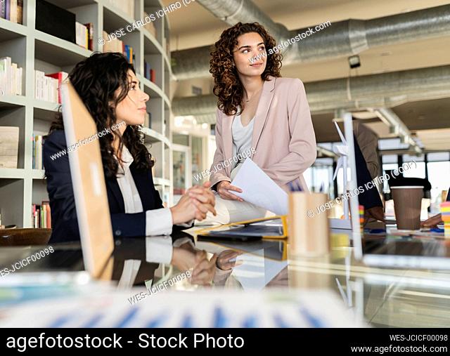 Businesswoman sitting on table with colleague in meeting at office