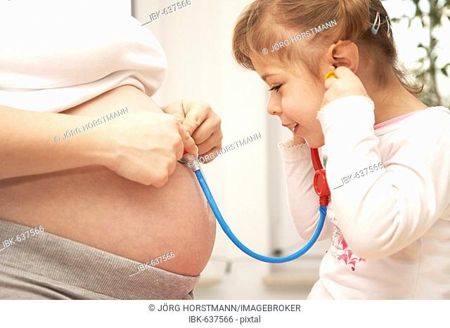 Four-year-old daughter holding a stethoscope to her mother's pregnant belly