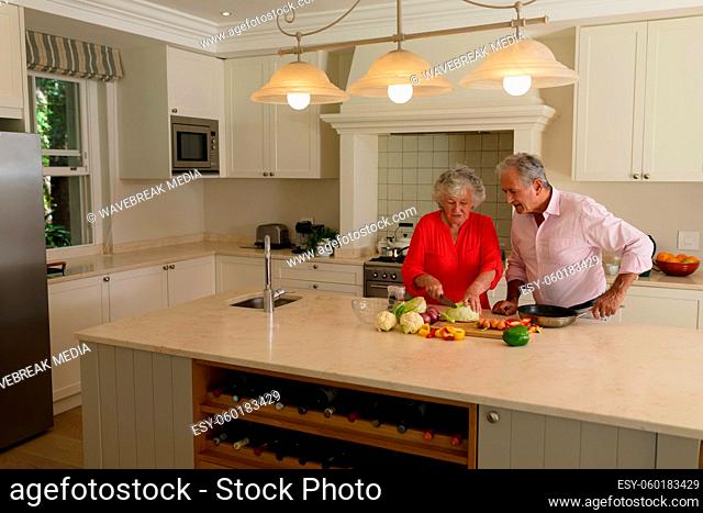 Senior caucasian couple cooking together and talking in kitchen