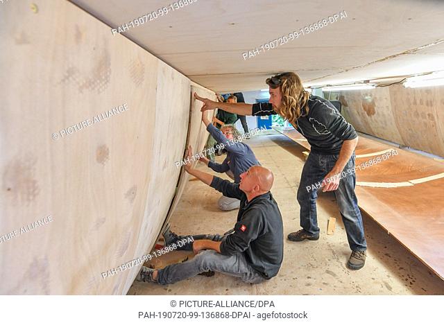 16 July 2019, Brandenburg, Kienitz-Nord: Morgan Briand (r), Vice President of the organization FYD-Adventure and several helpers are working in a hall on the...