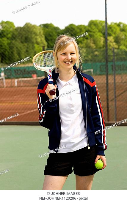 Young woman holding tennis racquet and ball, smiling, portrait