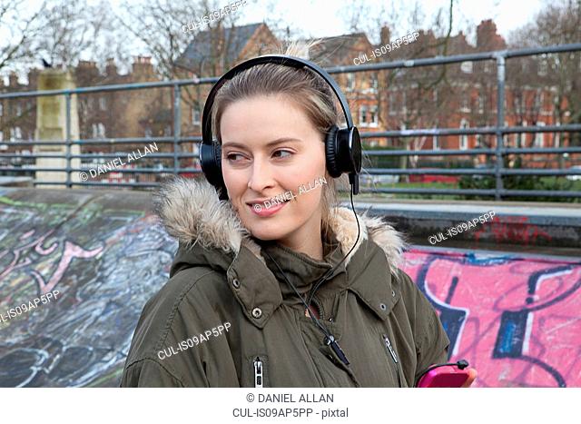 Young woman listening to headphone music in skatepark