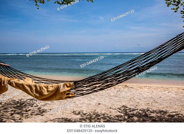 A towel in an empty hammock, swinging over the sand on a tropical beach, close to the sea, Gili Trawngan, Indonesia, April 25, 2018
