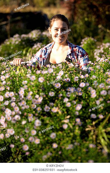 Beautiful smiling woman pruning flowers at garden with shears