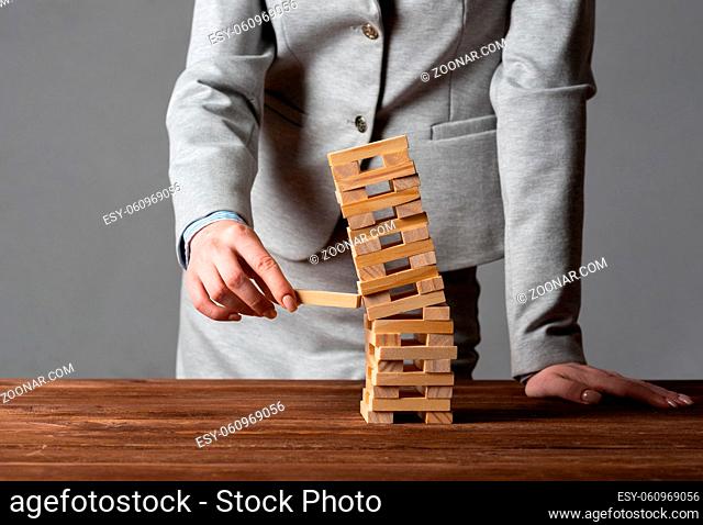 Businesswoman removing wooden block from falling tower on table. Management of risks and economic instability concept with wooden jenga game