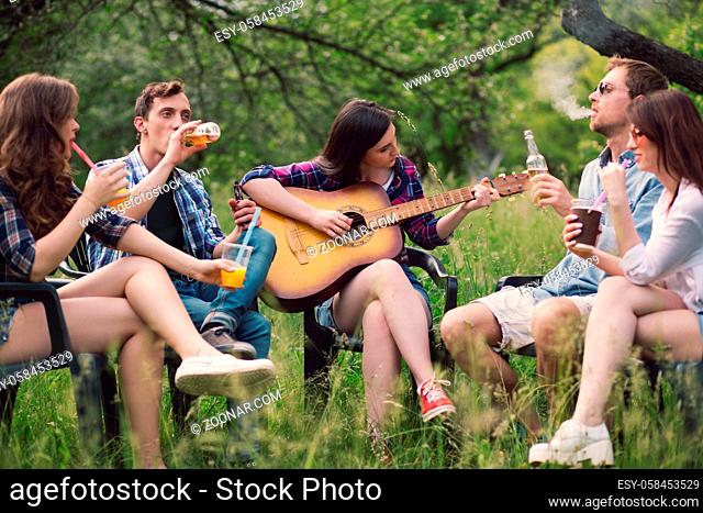 Group of friends hanging out in park. Friends having calm time in park sitting in circle playing some guitar music