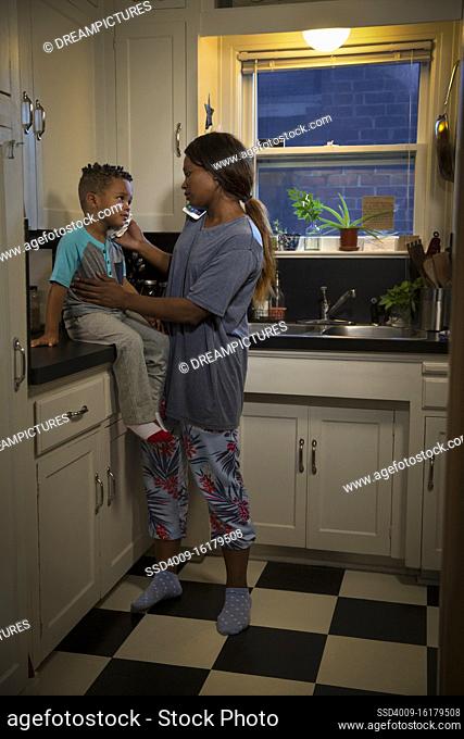 Mom at home in kitchen with son sitting on counter checking his temperature while talking to doctors on the phone