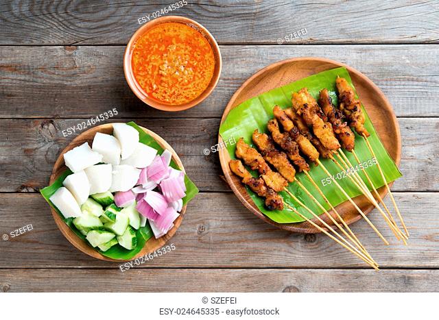 Overhead view Malaysian chicken sate with delicious peanut sauce, ketupat, onion and cucumber on wooden dining table, one of famous local dishes