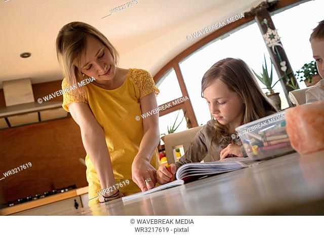 Mother helping children with homework in kitchen