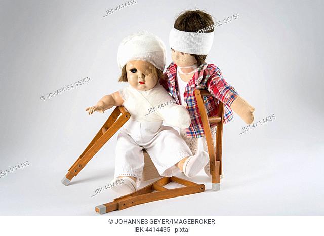 Two dolls, bandages on head, eye patch, arm and shoulder bandage, neck brace, crutches, white background