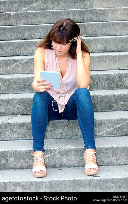 jungen Frau sitzt auf einer Treppe und liest im e-reader, Köln, Nordrhein-Westfalen, Deutschland
