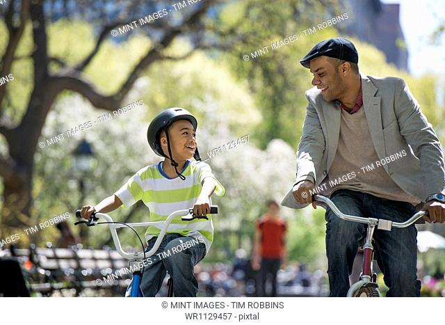 A family in the park on a sunny day. Bicycling and having fun. A father and son side by side
