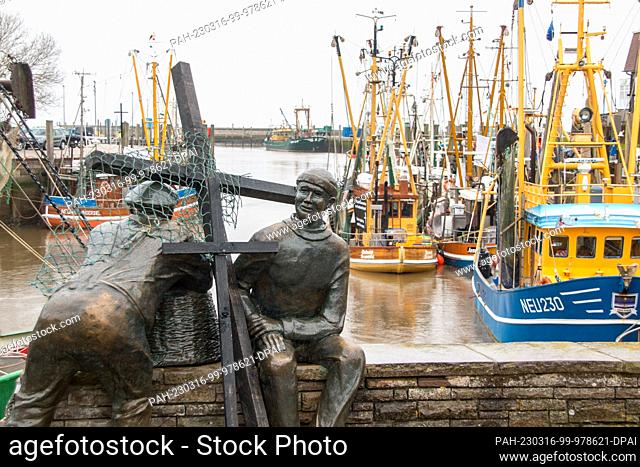 16 March 2023, Lower Saxony, Neuharlingersiel: Black wooden crosses lean against the bronze sculpture ""Old and Young Fishermen"" in the harbor on the occasion...