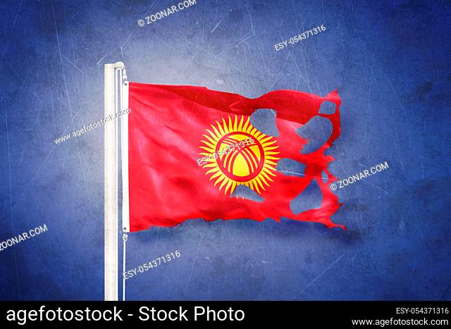 Torn flag of Kyrgyzstan flying against grunge background