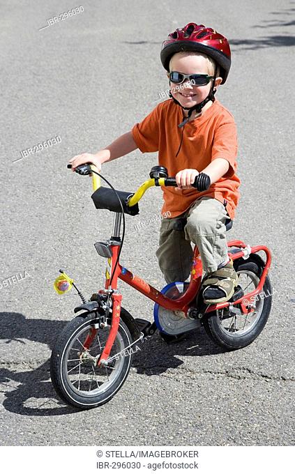 A boy, three years old, with a bicycle helmet and sunglasses on his bicycle