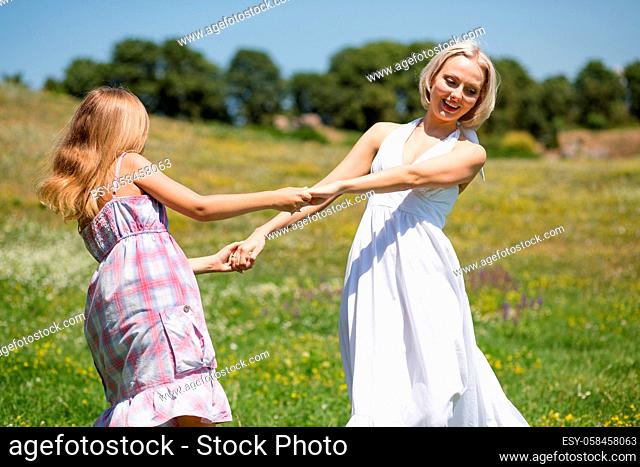 Mother and daughter dancing in a meadow. Happy family, mom and small daughter spending time outdoors