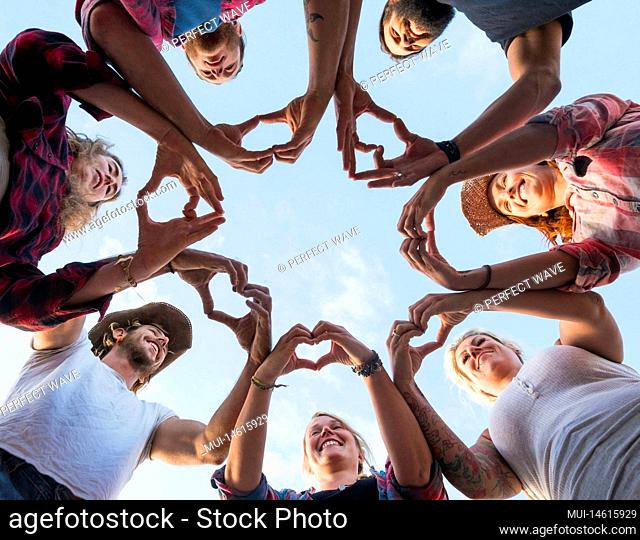 group of seven people together doing an heart with their fingers and hands - people in cricle having fun and playing - ground view