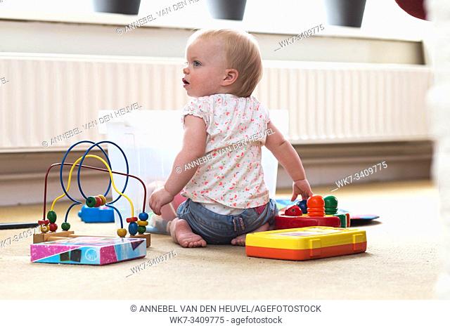 Baby playing alone with toys on a carpet on the floor at home messy