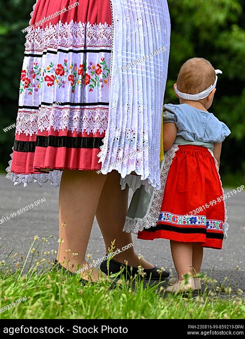 12 August 2023, Brandenburg, Heinersbrück: A mother in Sorbian-Wendish festive costume stands with her young daughter on the edge of the village and harvest...